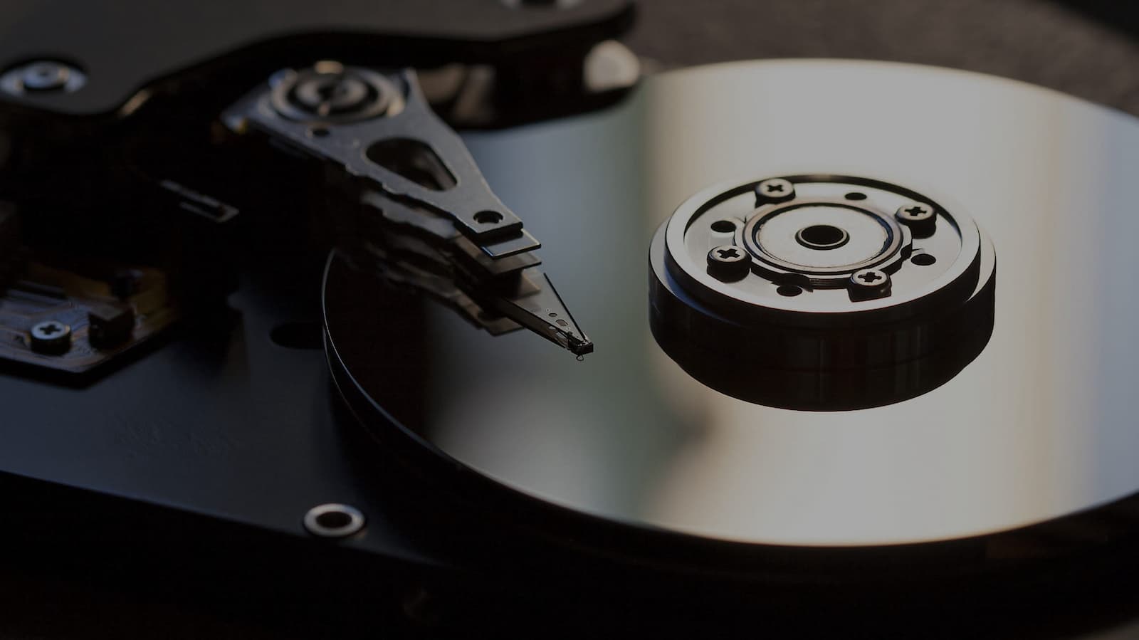 Close-up of an open hard disk drive, showing its reflective metallic platter and read/write head. The intricate components highlight the precision of data storage technology, with dark and shiny surfaces catching ambient light, a stark contrast to the finality of secure shredding services.